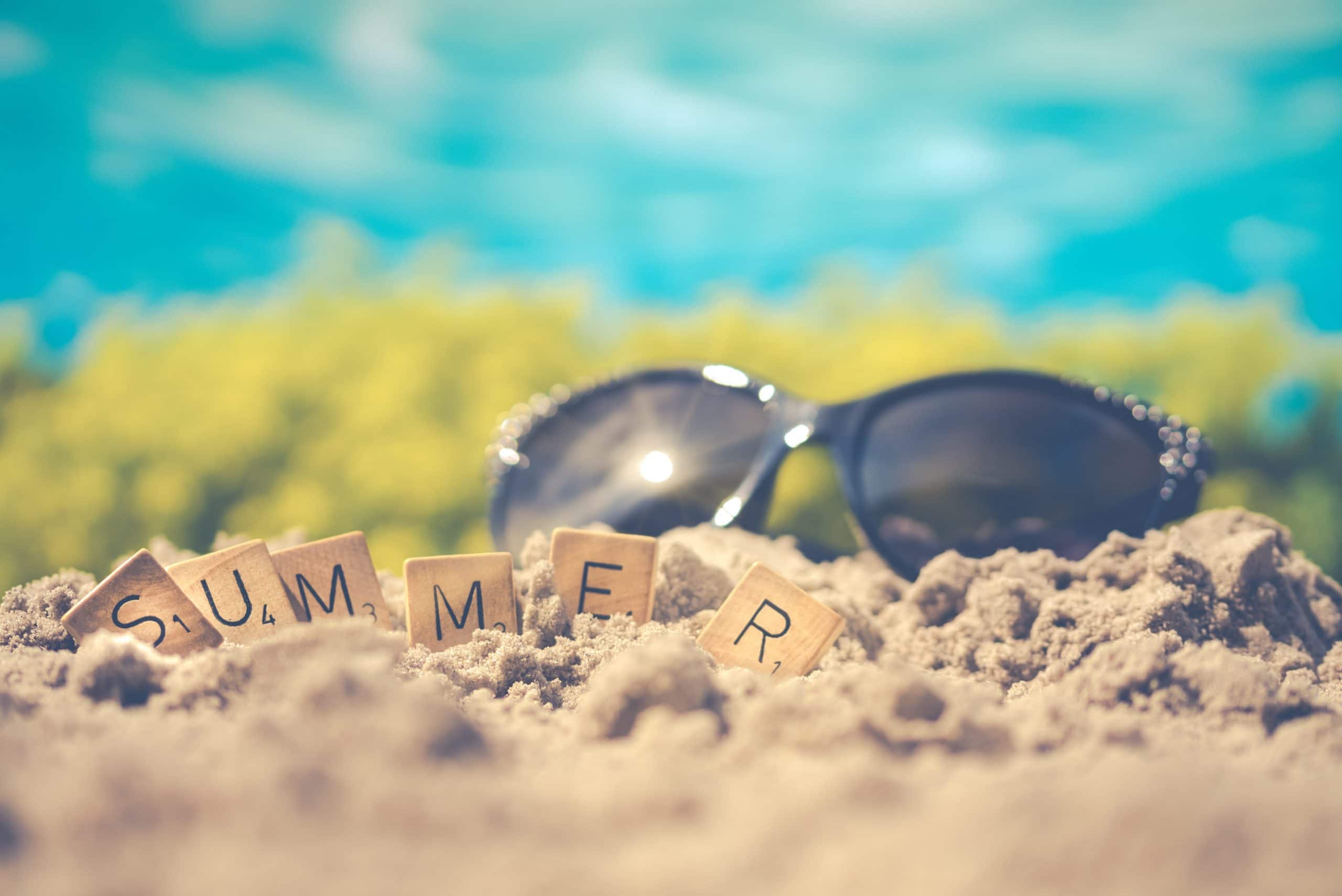 Sunglasses on sand with letters spelling “summer”