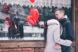 Couple with heart balloons embracing in front of shop window