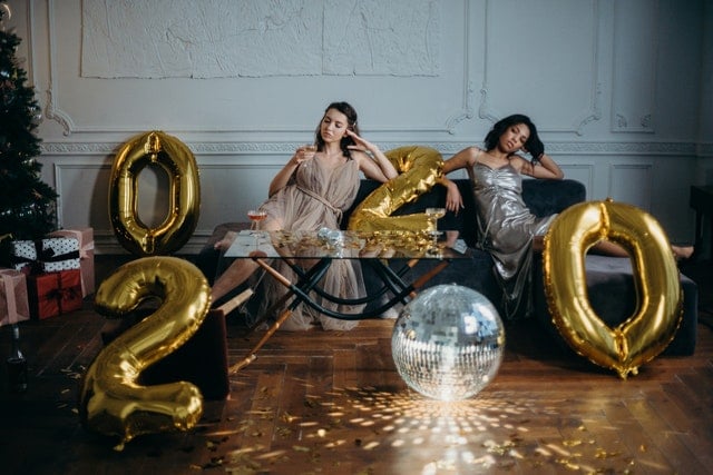 Bored women lounging on couch in room with 2020 balloons and mirror ball
